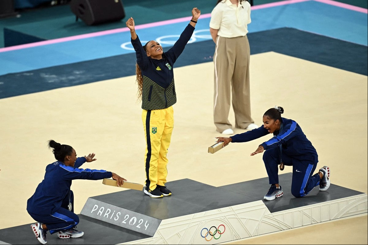 A ginasta brasileira Rebeca Andrade é reverenciada pelas norte-americanas Simone Biles e Jordan Chile após conquistar medalha de ouro no solo da ginástica artística no dia 5 de agosto