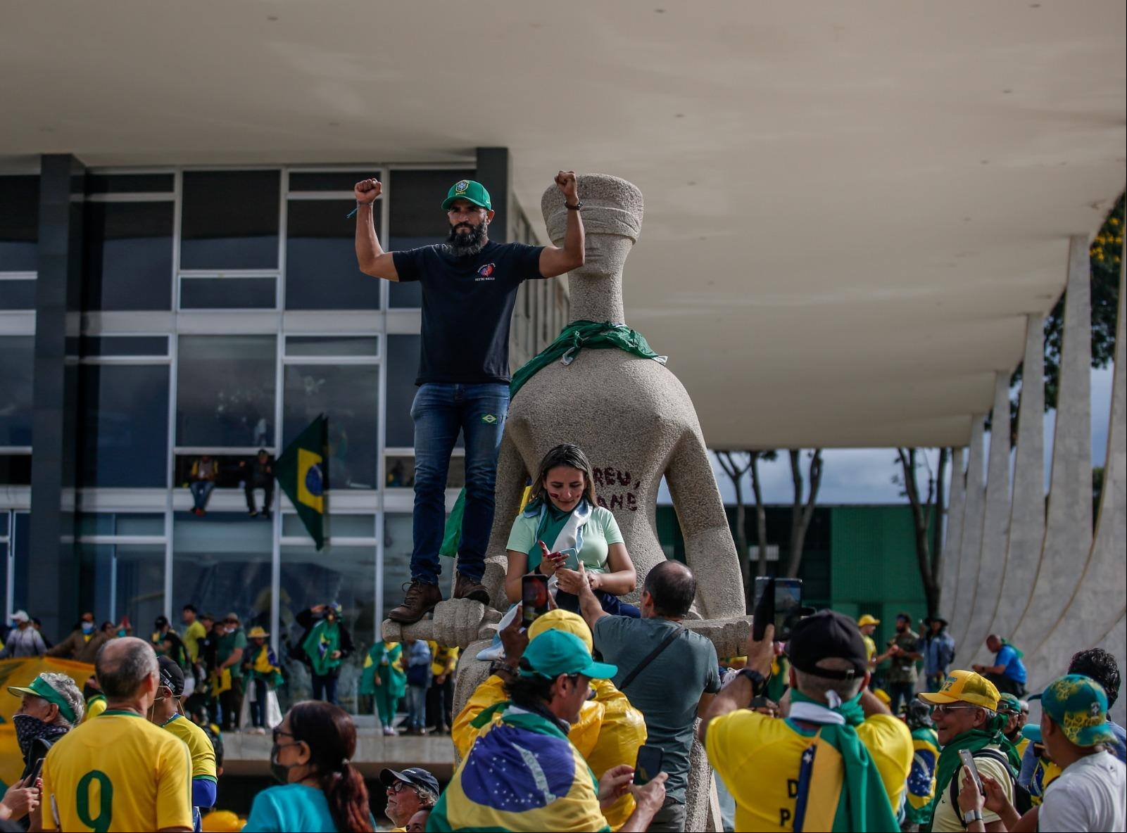 Mulher aparece sentada sob a estátua da Justiça pichada com "perdeu, mané" durante os atos criminosos de 8 de janeiro